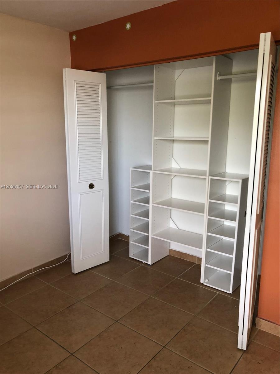 A closet with white shelving and louvered doors is set against a tiled room wall — 3808 SW 79th Ave # 63, Miami FL 33155, MIAMI, FL