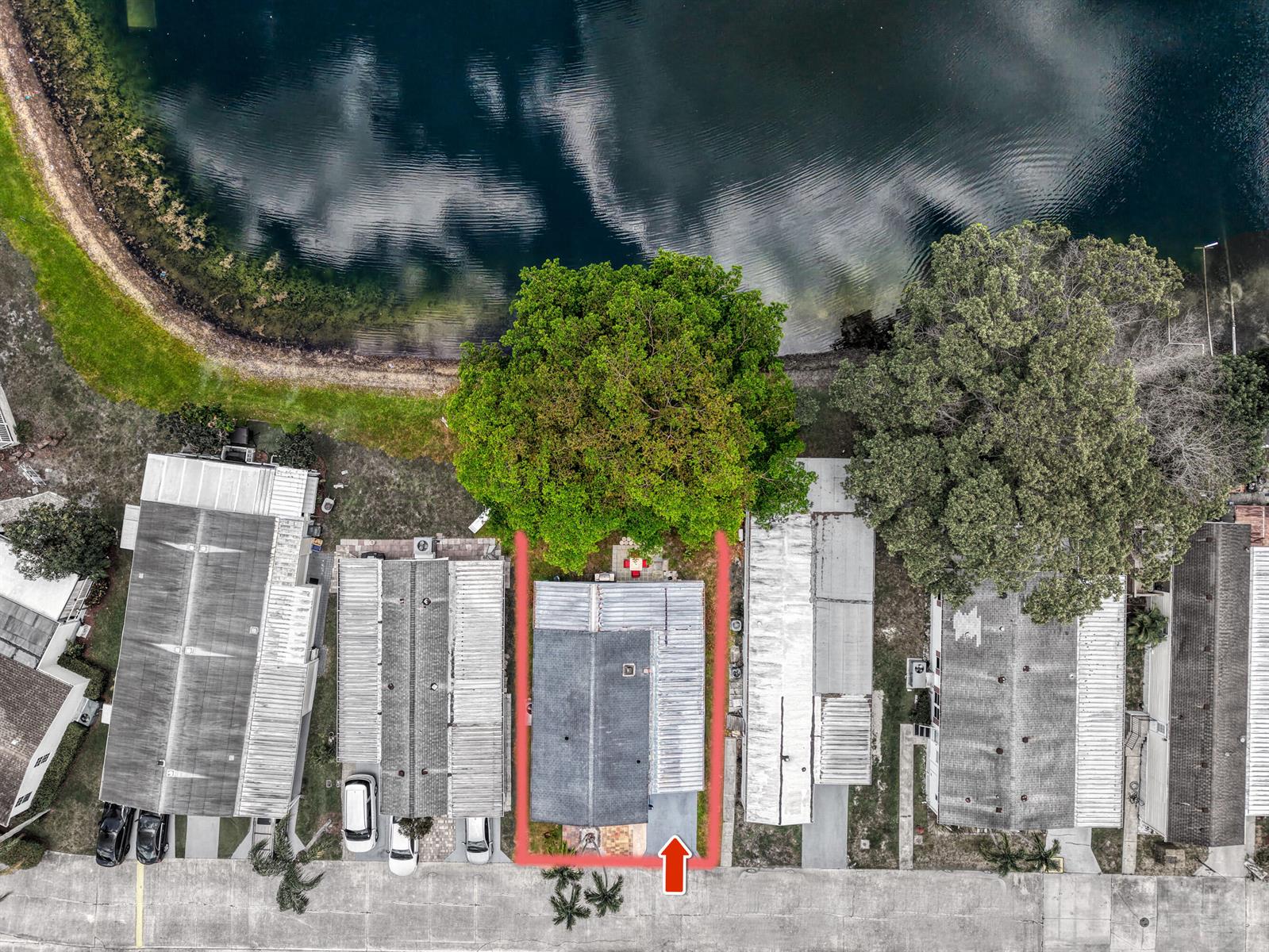 An aerial view shows a house with a red outline situated next to a lake — 141 Plantation Boulevard, Lake Worth FL 33467, LAKE WORTH, FL