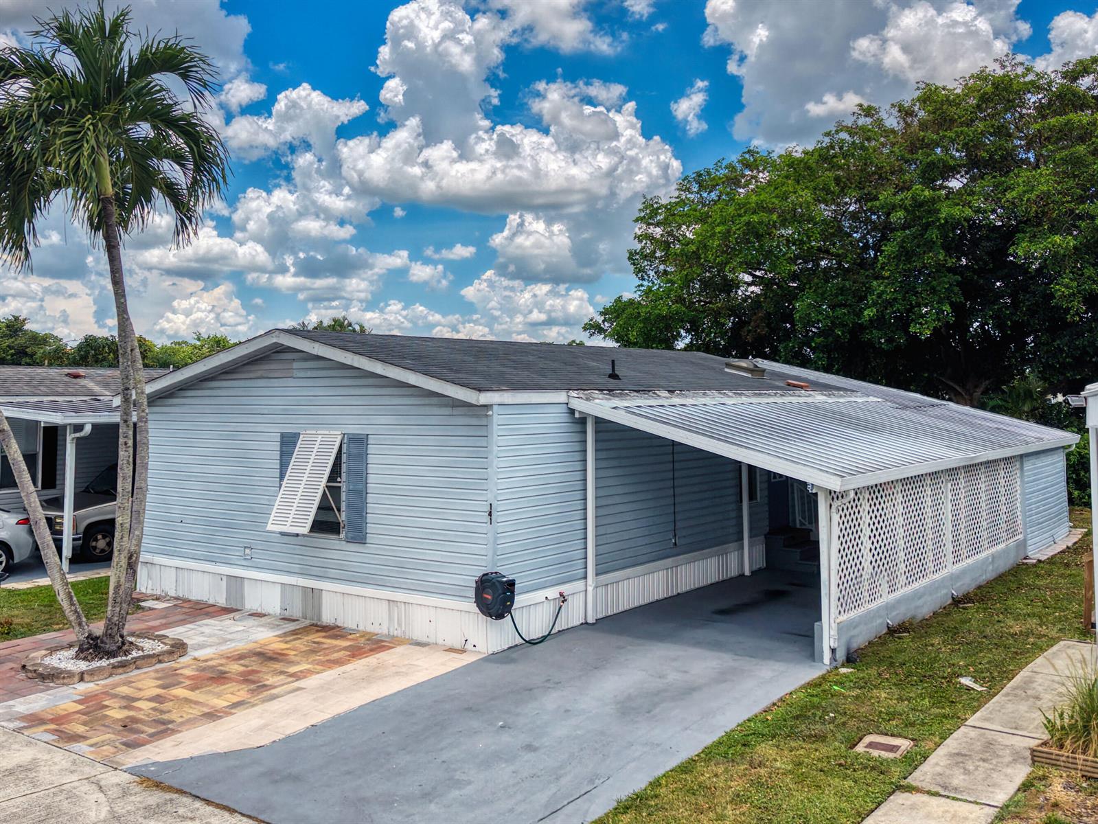 A light blue mobile home with a carport, lattice screen, and a palm tree — 141 Plantation Boulevard, Lake Worth FL 33467, LAKE WORTH, FL