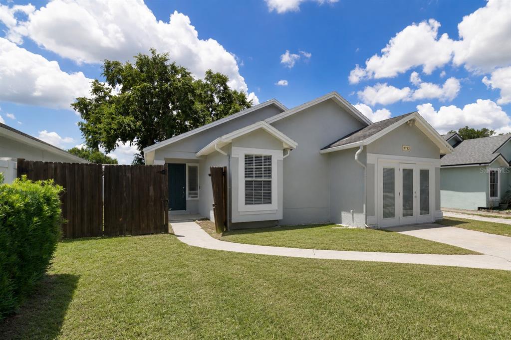 A single-story gray house with a front lawn, a concrete walkway, and a wooden fence — 9752 PINEY POINT CIRCLE, ORLANDO, FL