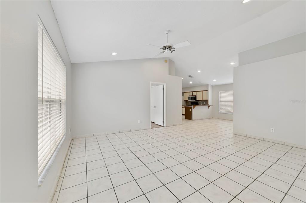 A spacious living room with white tile floors, a vaulted ceiling, and an open kitchen — 9752 PINEY POINT CIRCLE, ORLANDO, FL