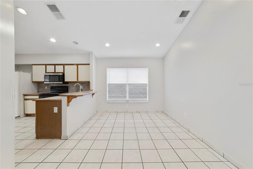 A kitchen with wooden cabinets and a breakfast bar opens to a tiled dining area — 9752 PINEY POINT CIRCLE, ORLANDO, FL