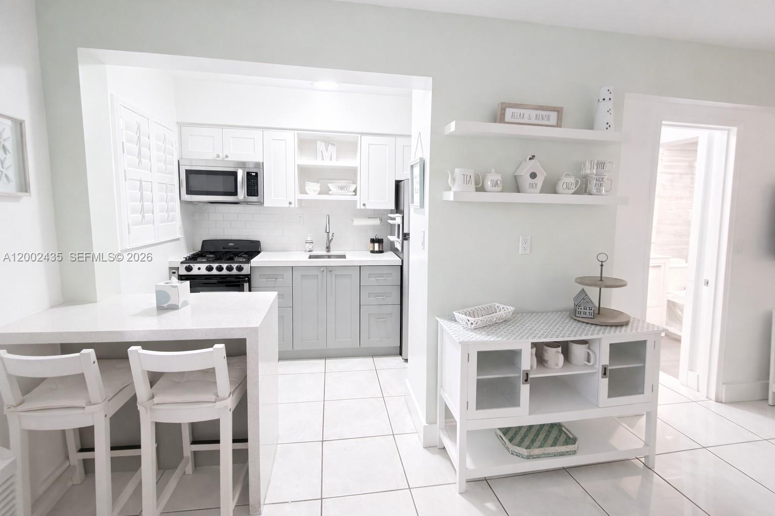 A kitchen features white cabinets, gray lower cupboards, a breakfast bar, and open wall shelving — 321 Wilson St # A105, Hollywood FL 33019, HOLLYWOOD, FL