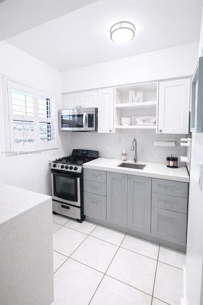 A kitchen features white upper cabinets, gray lower cabinets, stainless steel appliances, and white tile flooring — 321 Wilson St # A105, Hollywood FL 33019, HOLLYWOOD, FL