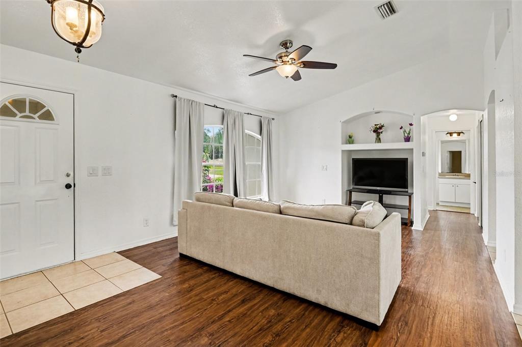 A living room features wood-look flooring, a beige sofa, a ceiling fan, and a television — 2638 ASHLAND LANE, NORTH PORT, FL