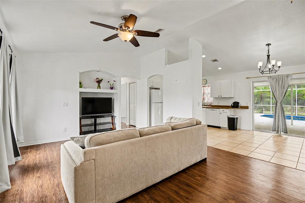 A living room with wood-look flooring, a beige sofa, and an adjacent tiled kitchen area — 2638 ASHLAND LANE, NORTH PORT, FL