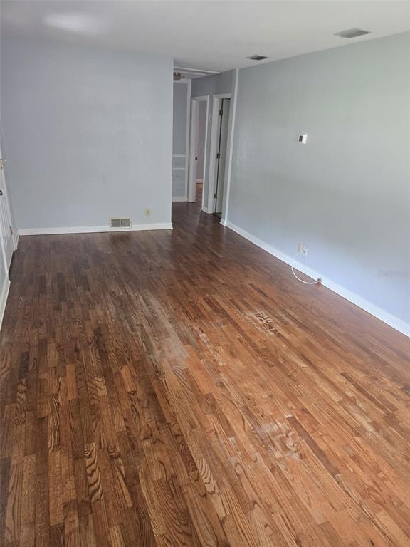 An empty room features light gray walls, hardwood flooring, and a doorway leading to a hallway — 659 N KEPLER ROAD, DELAND, FL