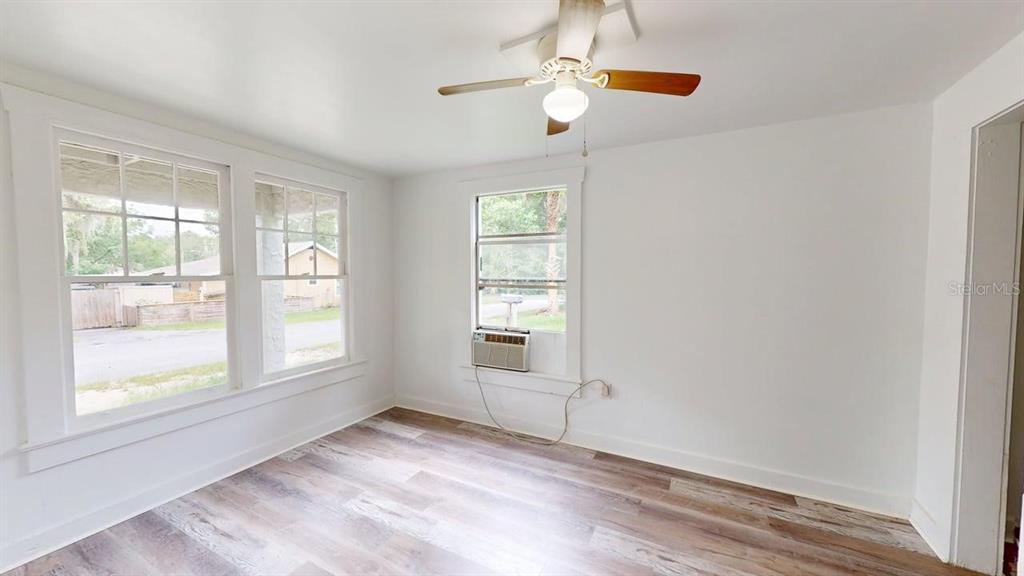 An empty room features wood-look flooring, a ceiling fan, and a window air conditioning unit — 738 WOOD STREET UNIT 1, DELAND, FL