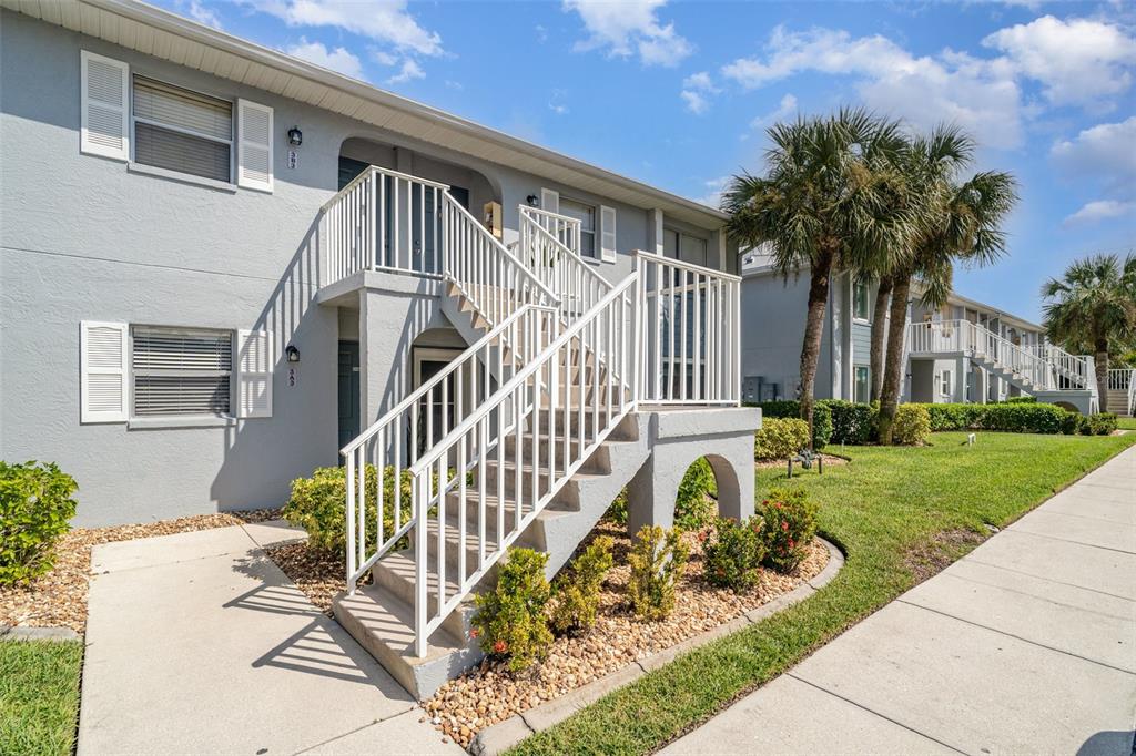 A two-story apartment building features white exterior stairs leading to an upper-level balcony — 25050 SANDHILL BOULEVARD UNIT A4, PUNTA GORDA, FL