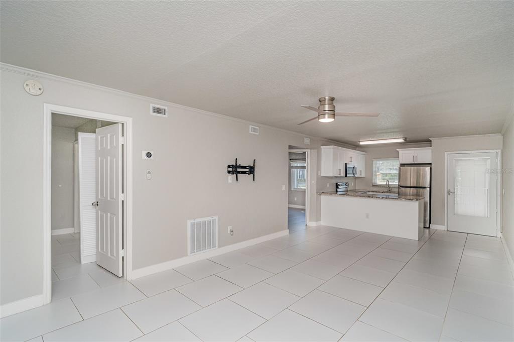 A bright, open-concept living area features light gray walls, white tile flooring, and a kitchen — 25050 SANDHILL BOULEVARD UNIT A4, PUNTA GORDA, FL