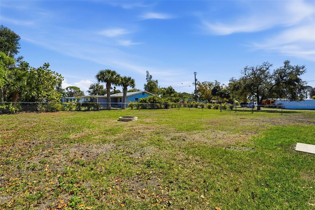 A large, grassy backyard features a fire pit, a chain-link fence, and surrounding trees — PALMETTO STREET, NOKOMIS, FL