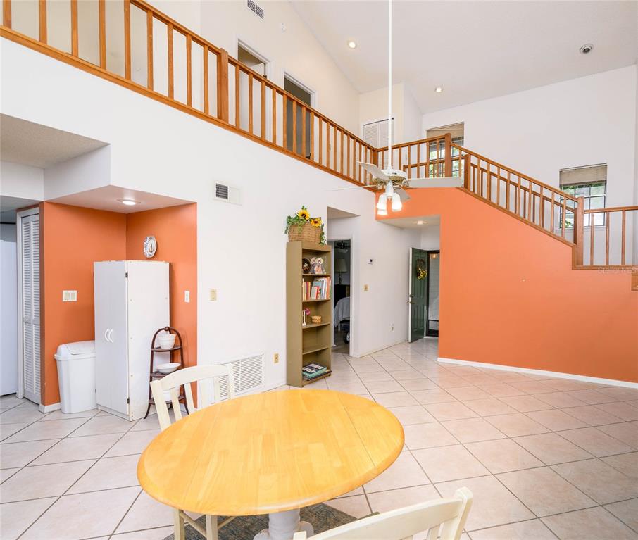 A dining area with a round wooden table sits before a staircase and orange walls — 4004 CROSSROADS PLACE, CASSELBERRY, FL