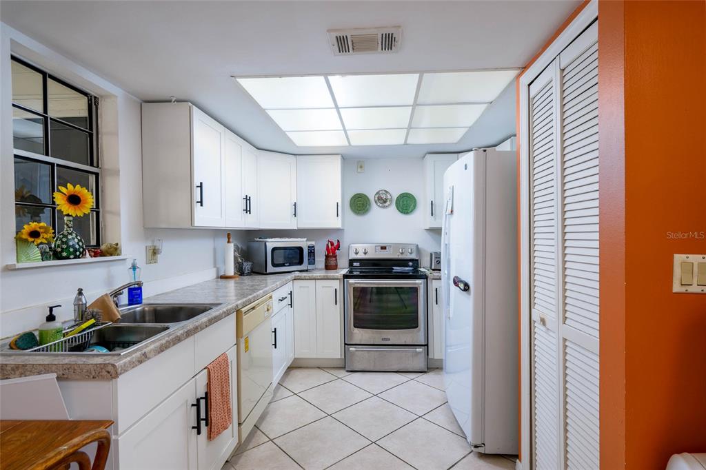 A kitchen features white cabinets, stainless steel appliances, a tiled floor, and a drop ceiling — 4004 CROSSROADS PLACE, CASSELBERRY, FL