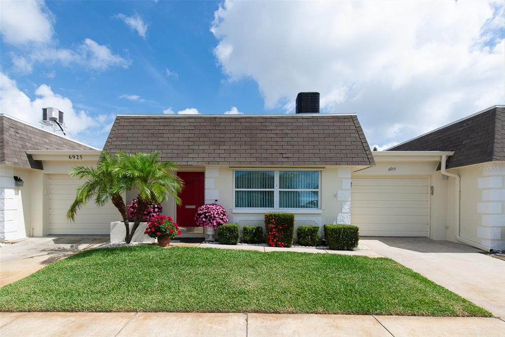 A single-story duplex with a red front door, a palm tree, and two garage doors — 6915 VERSAILLES N, PINELLAS PARK, FL