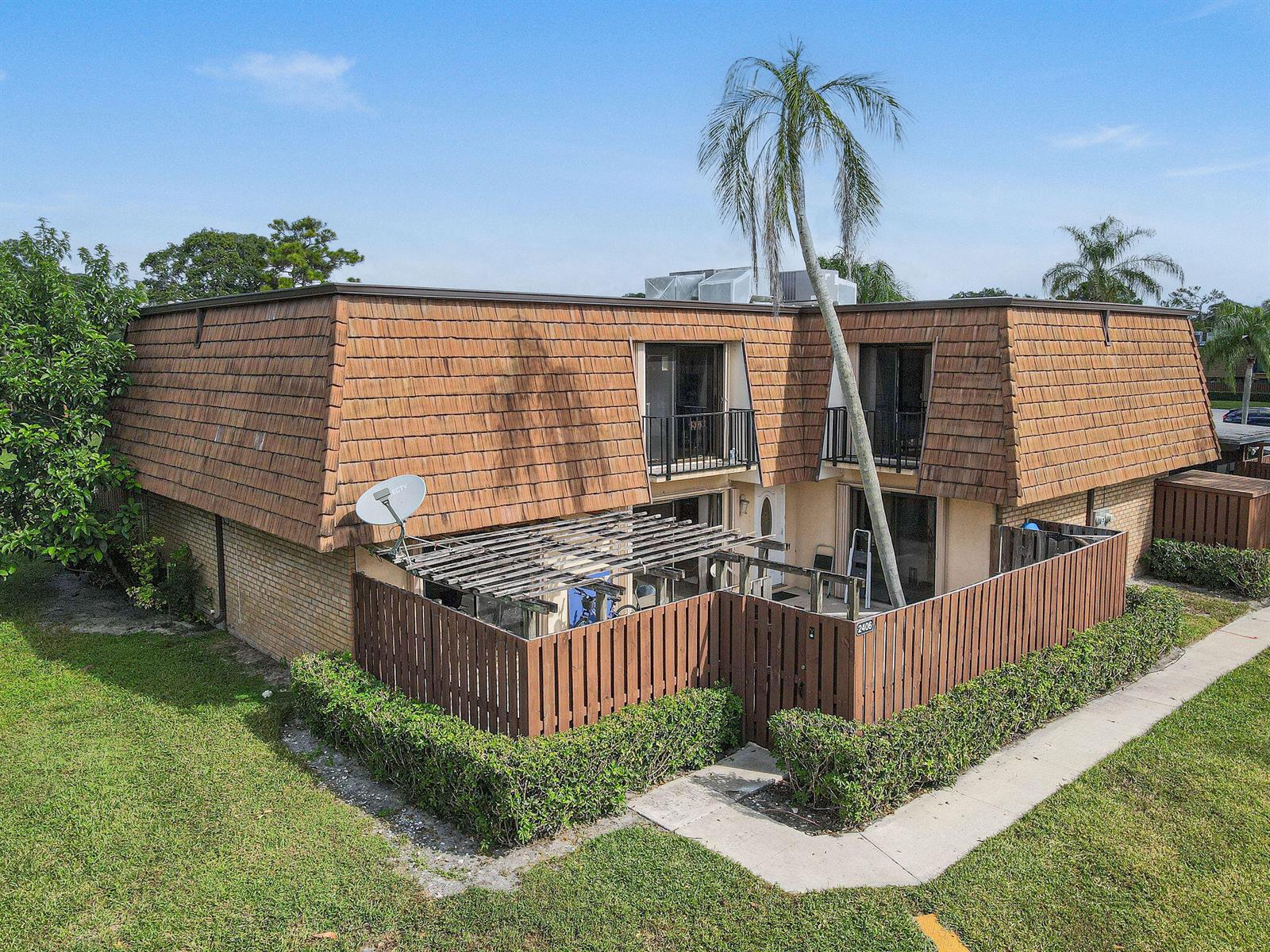 An exterior view of a two-story townhouse with a brown mansard roof and fenced patio — 2406 24th Lane, FL 33463, FL