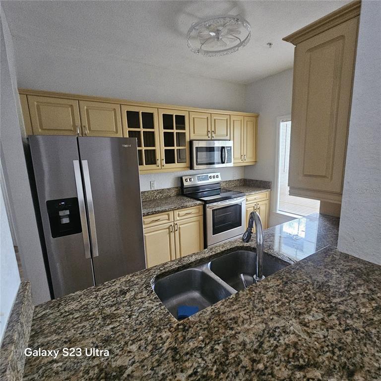 A kitchen features yellow cabinets, granite countertops, stainless steel appliances, and a double-basin sink — 3561 CONROY ROAD UNIT 220, ORLANDO, FL