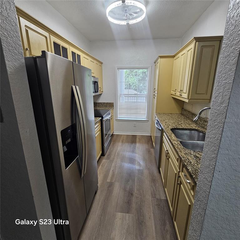 A galley kitchen features yellow cabinets, granite countertops, stainless steel appliances, and wood-look flooring — 3561 CONROY ROAD UNIT 220, ORLANDO, FL