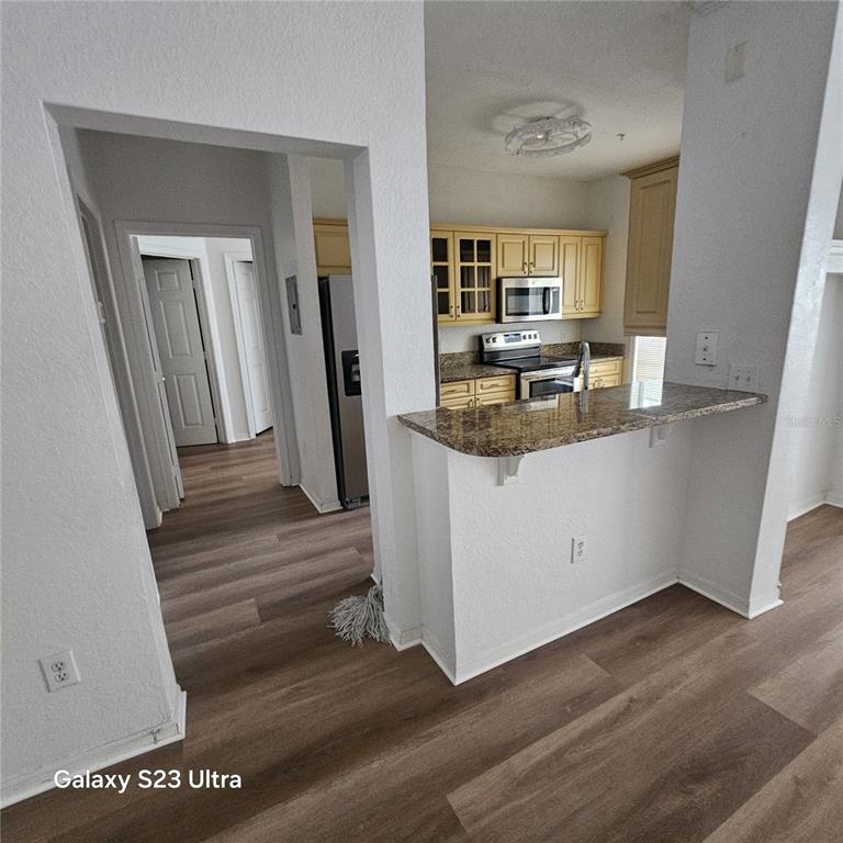 A kitchen with light wood cabinets and a granite breakfast bar overlooks a hallway — 3561 CONROY ROAD UNIT 220, ORLANDO, FL