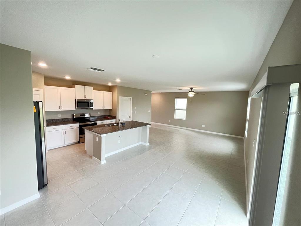 A kitchen with white cabinets and a granite island opens into a spacious living area — 31454 BARREL WAVE WAY, WESLEY CHAPEL, FL
