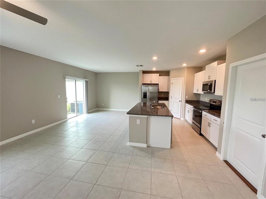 An open-concept kitchen and living area features tile flooring, a granite island, and white cabinetry — 31454 BARREL WAVE WAY, WESLEY CHAPEL, FL