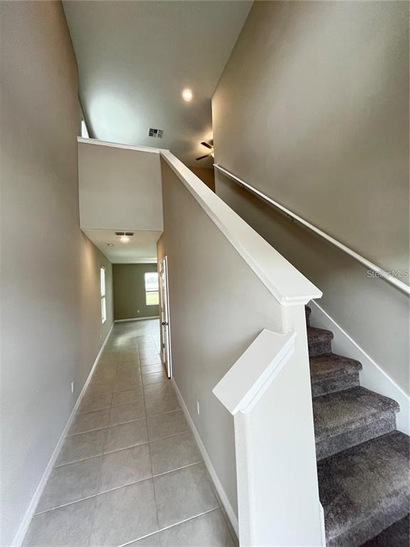 A hallway with tile flooring leads to a doorway, with carpeted stairs on the right — 31454 BARREL WAVE WAY, WESLEY CHAPEL, FL