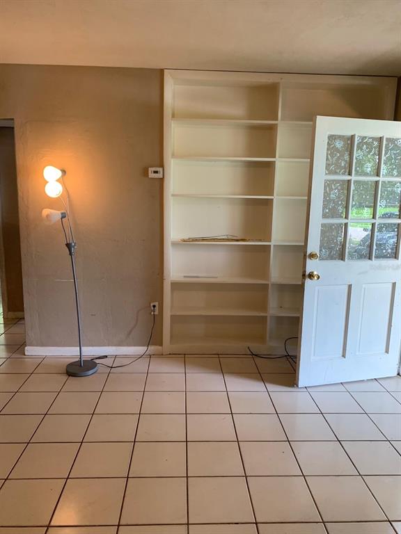 A room with tiled flooring, a floor lamp, and built-in white shelving next to a door — 21266 COULTON AVENUE, PORT CHARLOTTE, FL