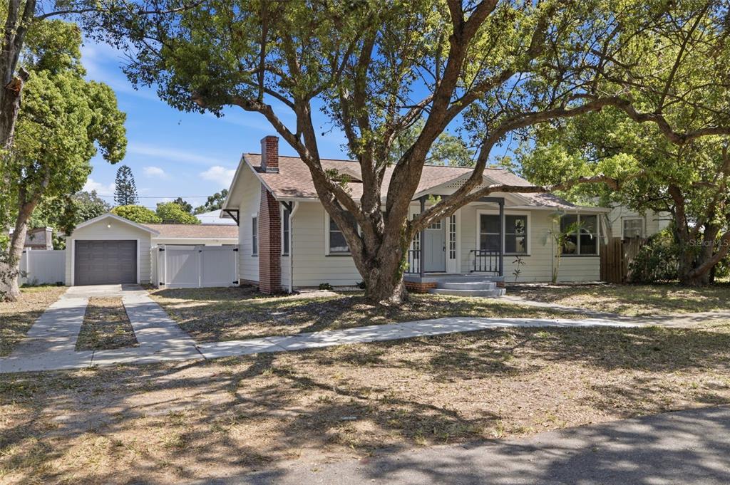 A single-story house with a brick chimney, front porch, and detached garage under large trees — 1235 IDLEWILD DRIVE, CLEARWATER, FL