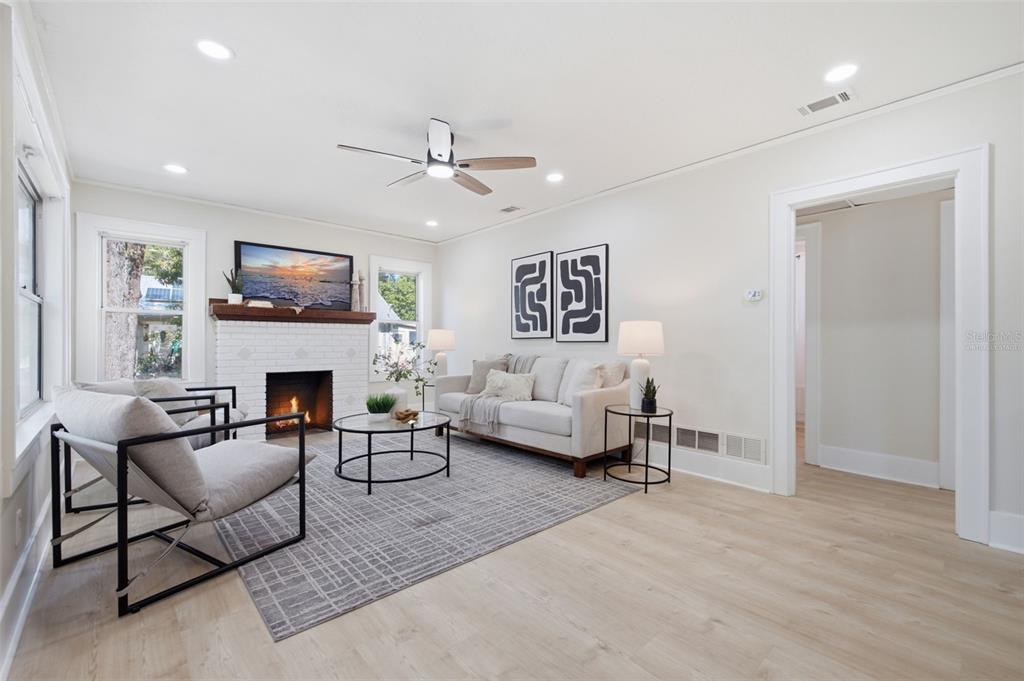 A living room features a white brick fireplace, light wood floors, and a gray area rug — 1235 IDLEWILD DRIVE, CLEARWATER, FL
