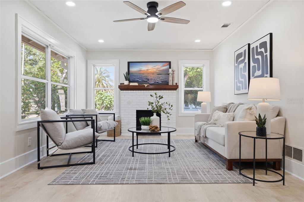 A bright living room features a white brick fireplace, a ceiling fan, and neutral furniture — 1235 IDLEWILD DRIVE, CLEARWATER, FL