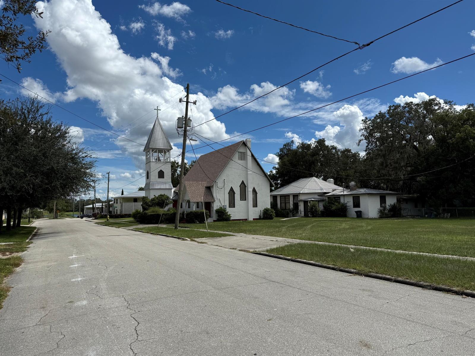 A white church with a steeple stands beside a grassy lawn along a paved street — 18 E Pleasant Street, FL 33825, FL