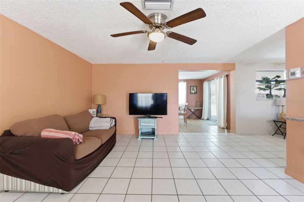 A living room with peach walls, white tile flooring, a brown sofa, and ceiling fan — 8829 EILEEN DRIVE, PORT RICHEY, FL