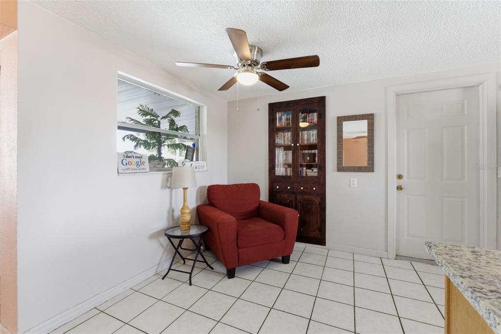 A room with white tile floors, a red armchair, a ceiling fan, and a wooden cabinet — 8829 EILEEN DRIVE, PORT RICHEY, FL