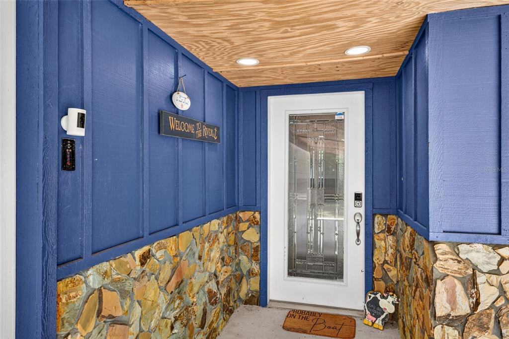 A front entryway features blue board-and-batten siding, stone wainscoting, a wood ceiling, and a door — 4600 S LEWOODS DRIVE, HOMOSASSA, FL