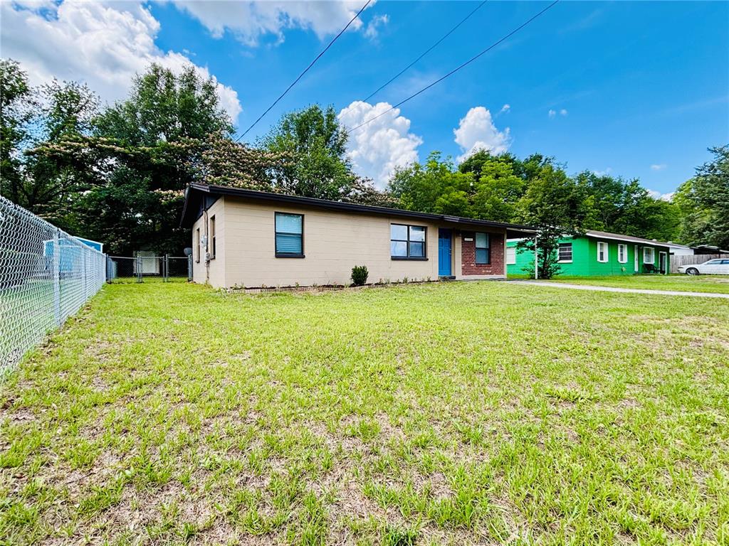 A single-story house with tan siding, a blue front door, and a chain-link fence — 13601 NW 141ST PLACE, ALACHUA, FL