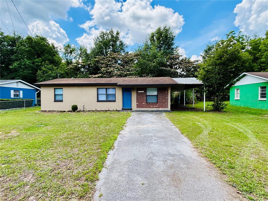 A single-story house with a tan exterior, brick accent, blue front door, and attached carport — 13601 NW 141ST PLACE, ALACHUA, FL