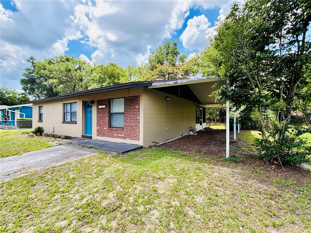 A single-story house with a brick facade, blue front door, and an attached carport — 13601 NW 141ST PLACE, ALACHUA, FL