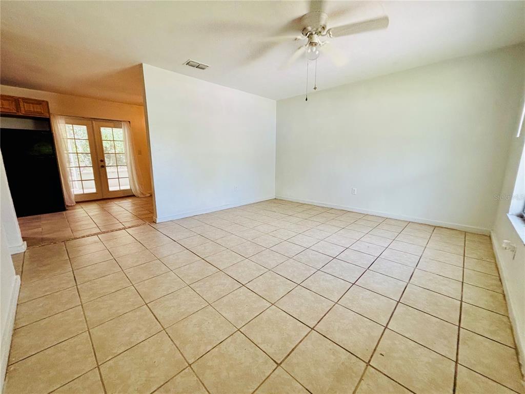 An empty room with beige tile flooring, a ceiling fan, and a glass door entrance — 13601 NW 141ST PLACE, ALACHUA, FL