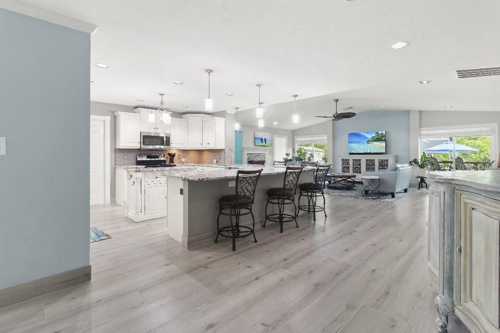 A modern open-concept kitchen features a large granite island, white cabinetry, and light wood flooring — 810 25TH AVENUE W, PALMETTO, FL
