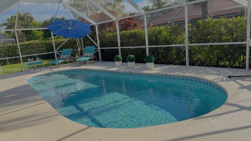 A swimming pool with a screen enclosure, patio furniture, and an umbrella in a backyard — 165 Cypress Trce, Royal Palm Beach FL 33411, ROYAL PALM BEACH, FL