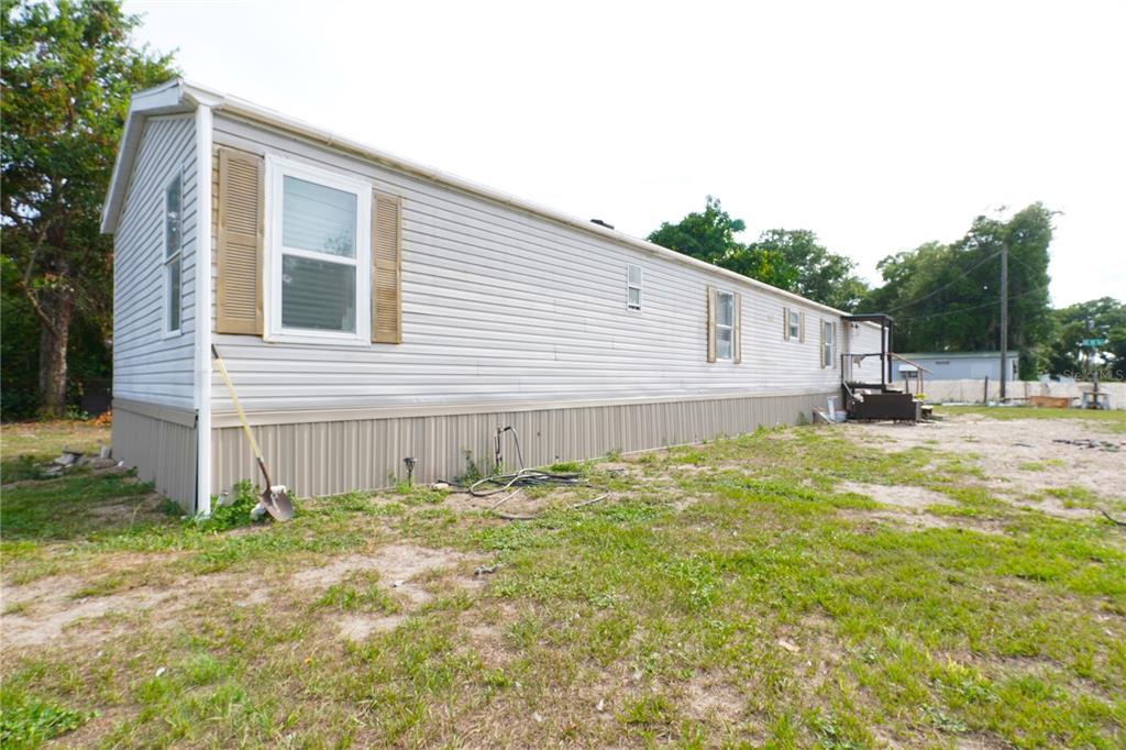 The exterior of a long, light-colored mobile home sits on a grassy, dirt-covered lot — 14041 SE 90TH TERRACE, SUMMERFIELD, FL