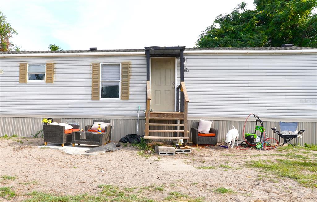Exterior view of a single-wide mobile home with light siding, a wooden staircase, and patio furniture — 14041 SE 90TH TERRACE, SUMMERFIELD, FL