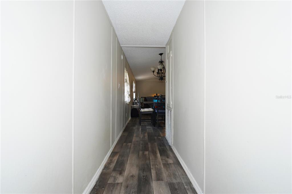 A narrow hallway with white paneled walls and dark wood-look flooring leads to a dining area — 14041 SE 90TH TERRACE, SUMMERFIELD, FL