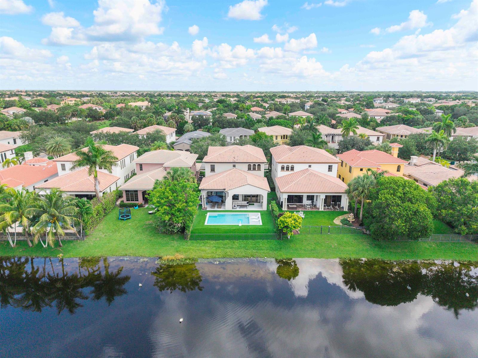 An aerial view shows suburban houses with tiled roofs, swimming pools, and backyards facing a lake — 9594 Ginger Court, Parkland FL 33076, PARKLAND, FL