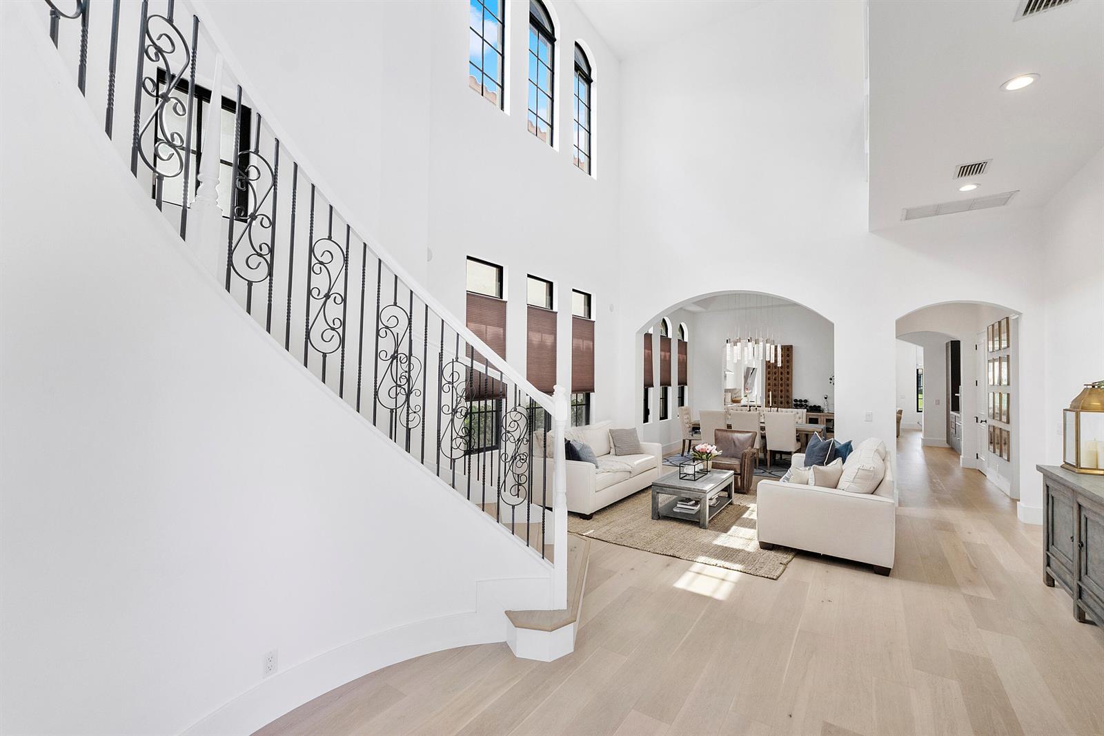 A bright, open-concept living room features a curved staircase, high ceilings, and light wood floors — 9594 Ginger Court, Parkland FL 33076, PARKLAND, FL