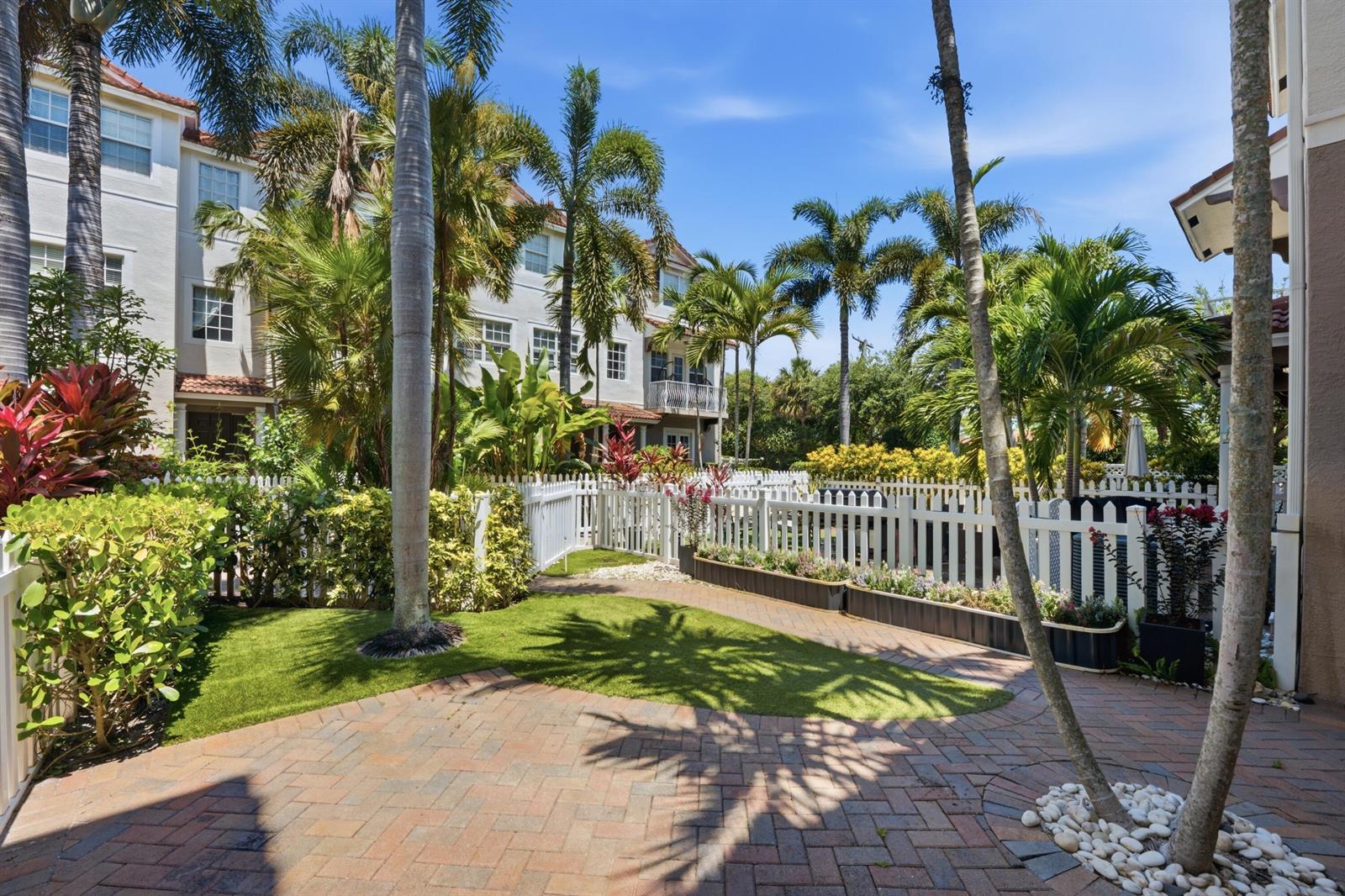 A brick patio leads to a small grassy yard enclosed by a white picket fence — 107 Ocean Cay Way, Hypoluxo FL 33462, HYPOLUXO, FL