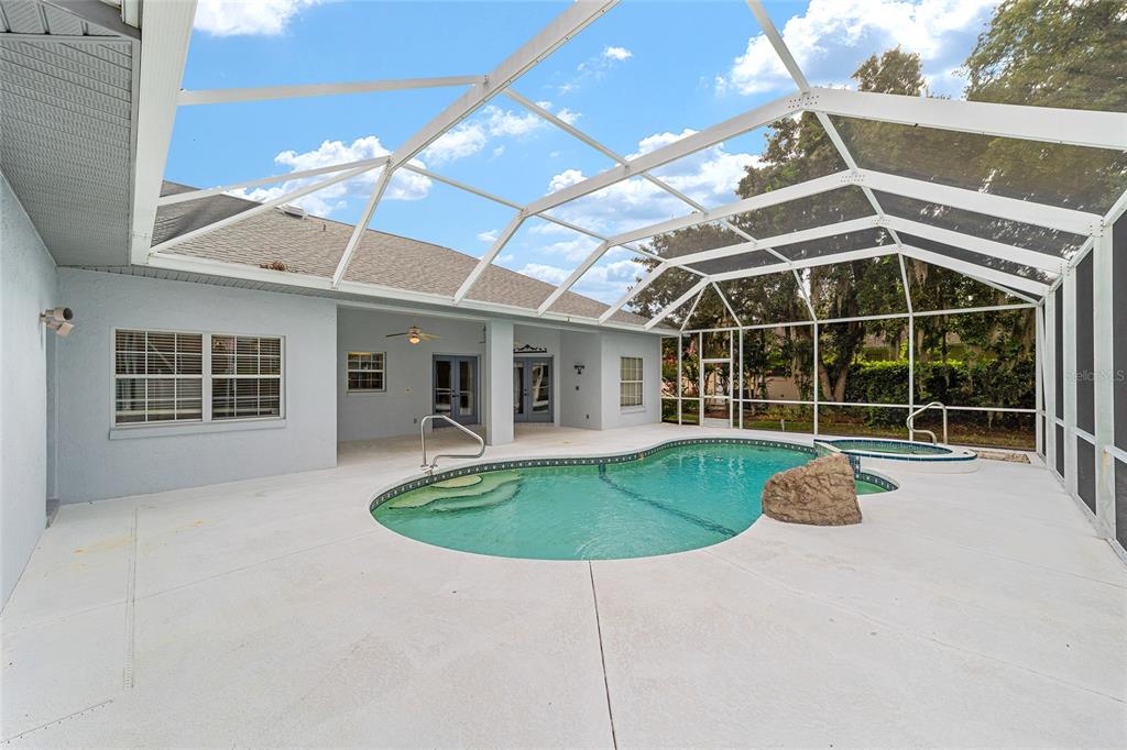 A screened-in patio features a swimming pool with a spa and a large decorative rock — 5366 SW 86TH PLACE, OCALA, FL