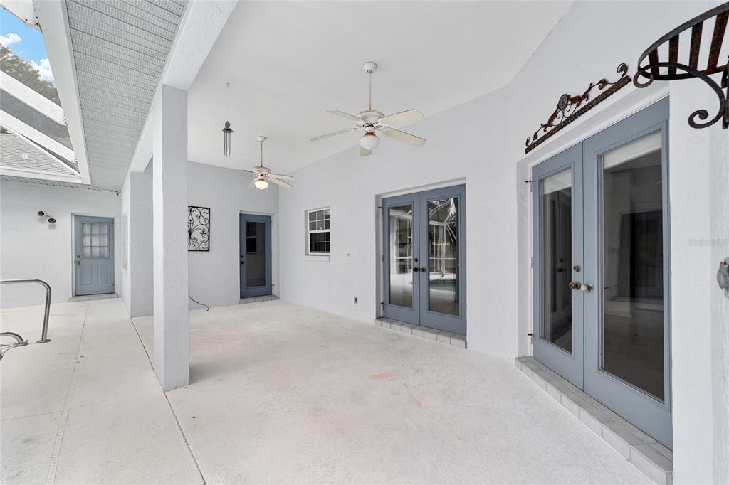 A covered outdoor patio features white walls, two ceiling fans, and multiple blue-framed glass doors — 5366 SW 86TH PLACE, OCALA, FL