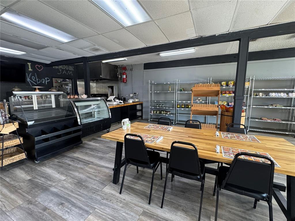A commercial kitchen and dining area features a wooden table, black chairs, and metal shelving — 1420 E FLETCHER AVENUE, TAMPA, FL