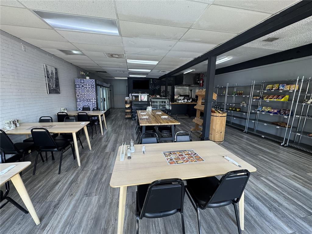 A restaurant dining area features light wood tables, black chairs, and metal shelving units — 1420 E FLETCHER AVENUE, TAMPA, FL