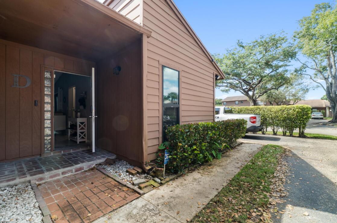 An exterior view of a brown wood-sided building with a brick entryway and open door — 6194 Pine Tree Lane # D, Tamarac FL 33319, TAMARAC, FL